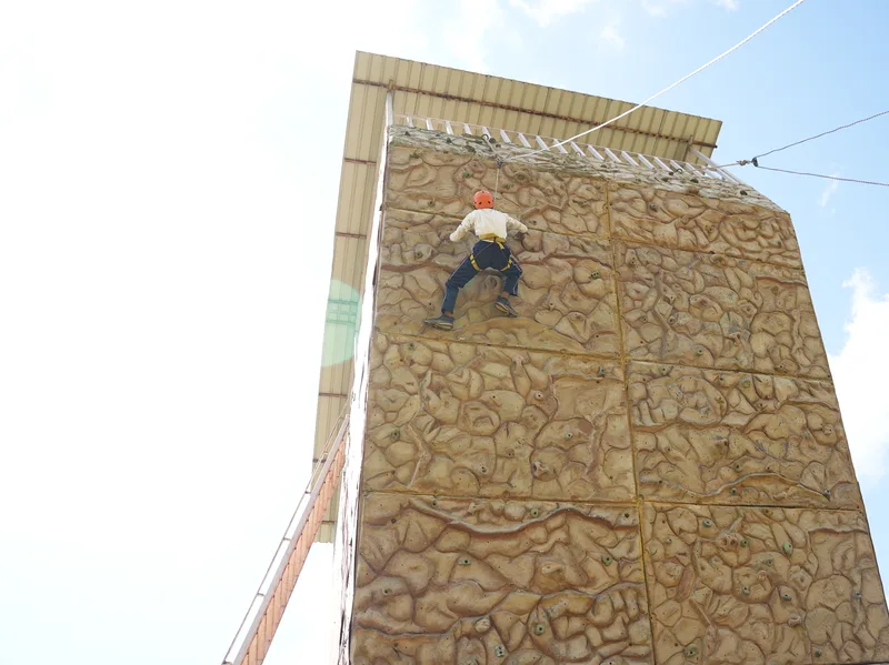 A climber on the ICE rock-climbing wall in Pithoragarh, roped and helmeted