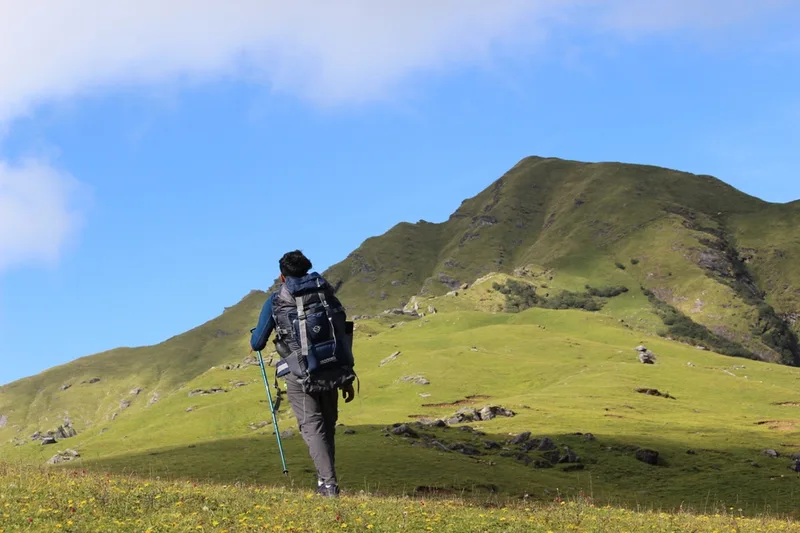 Trekker walking towards the green alpine meadow of Khaliya Top